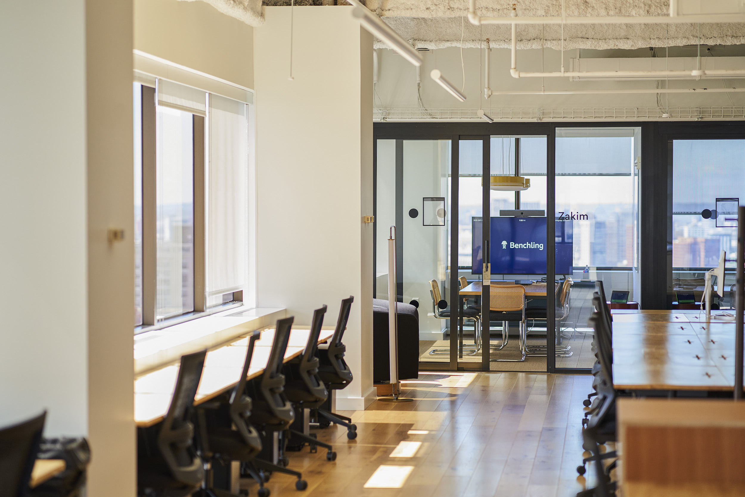 Office hallway looking into windowed conference room with TV screen that contains Benchling logo