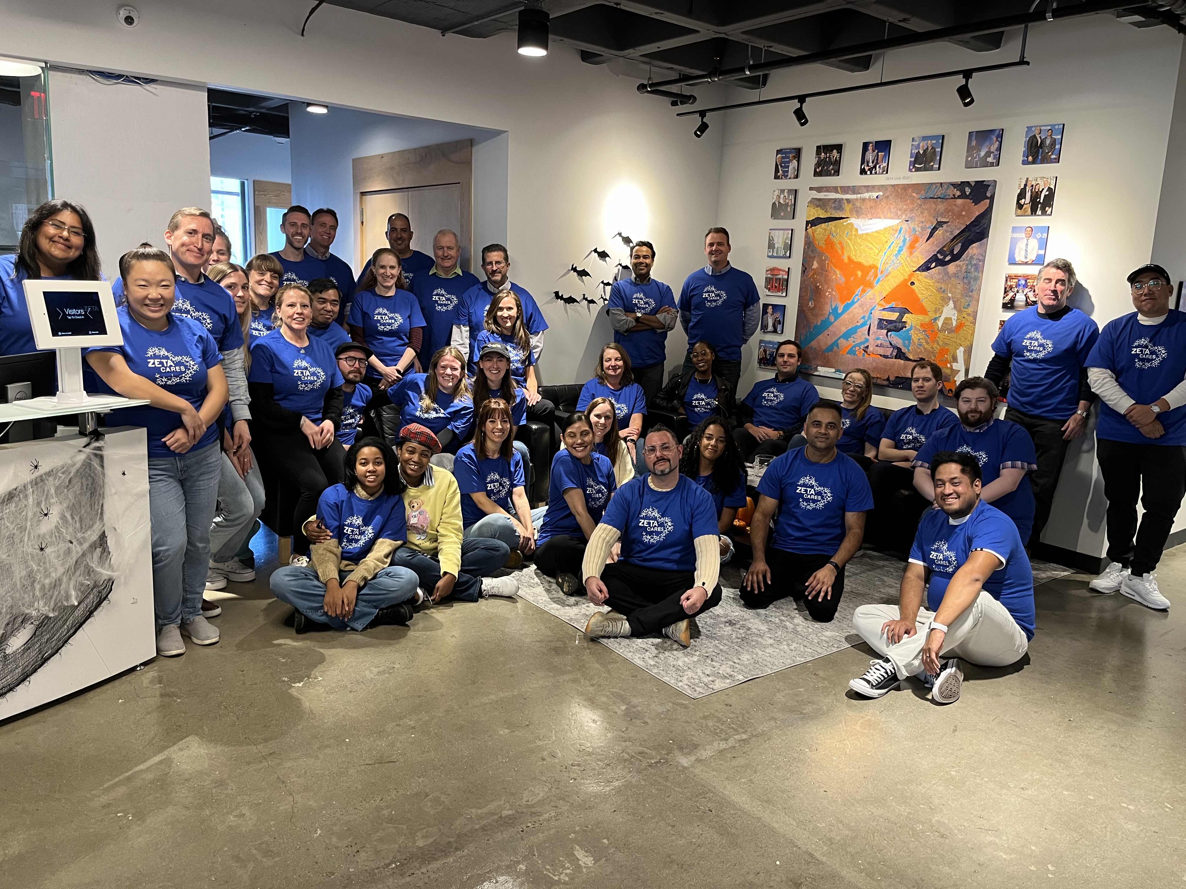 Zeta Global team members in branded blue T-shirts gather for a photo in the office