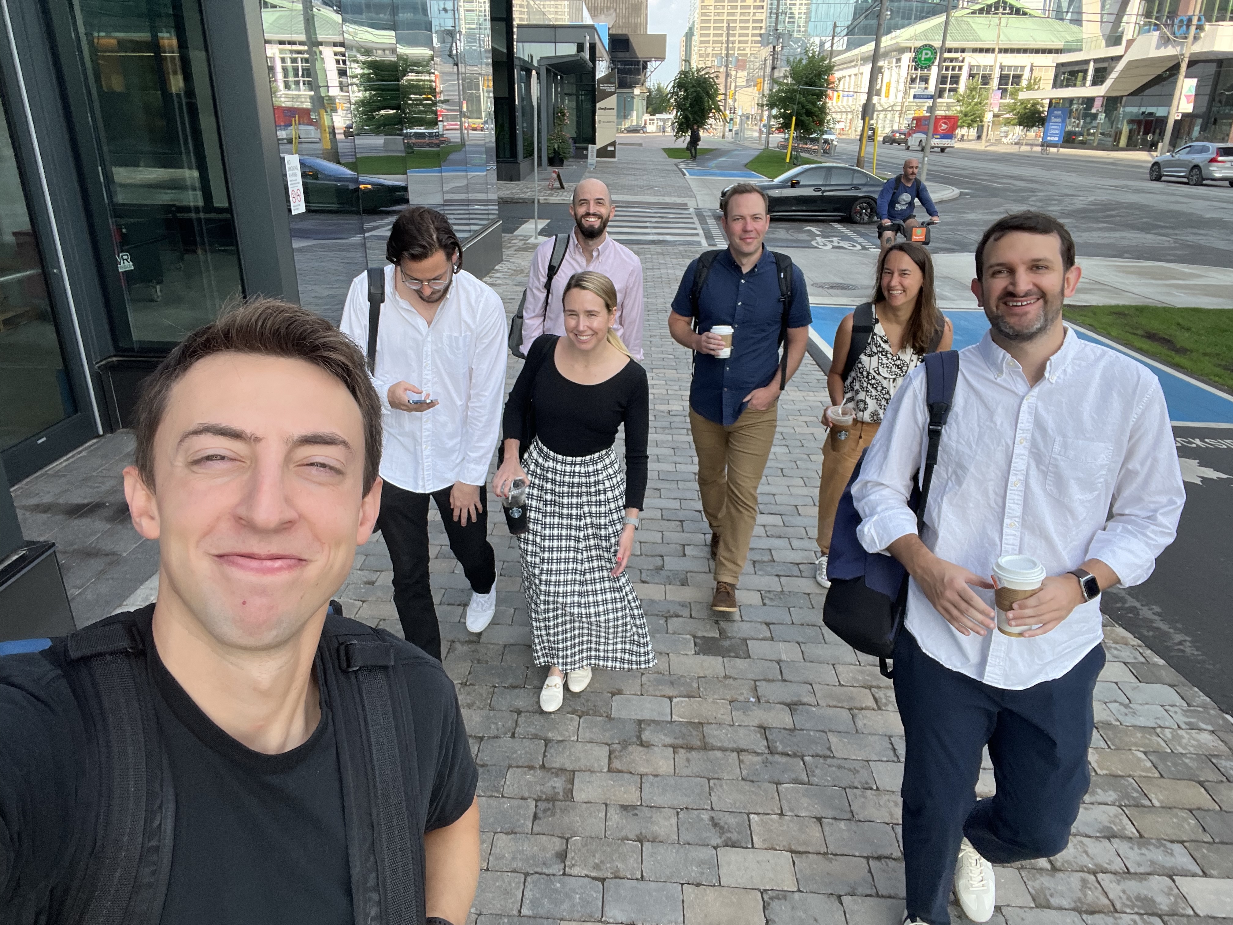 A group of Check employees are walking down a city street. One person is taking a selfie of the group.