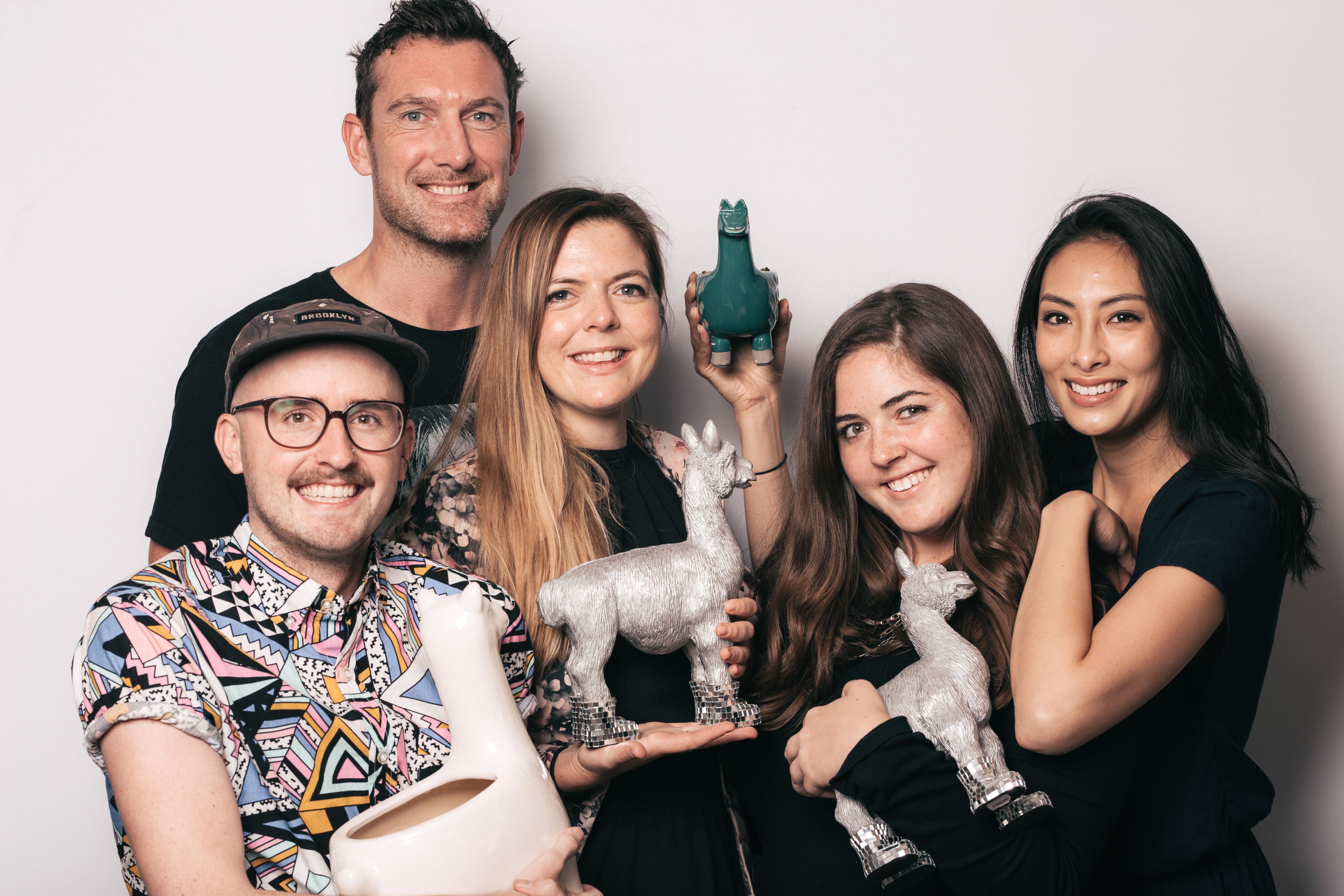 Group of five NextRoll team members holding llama statues.